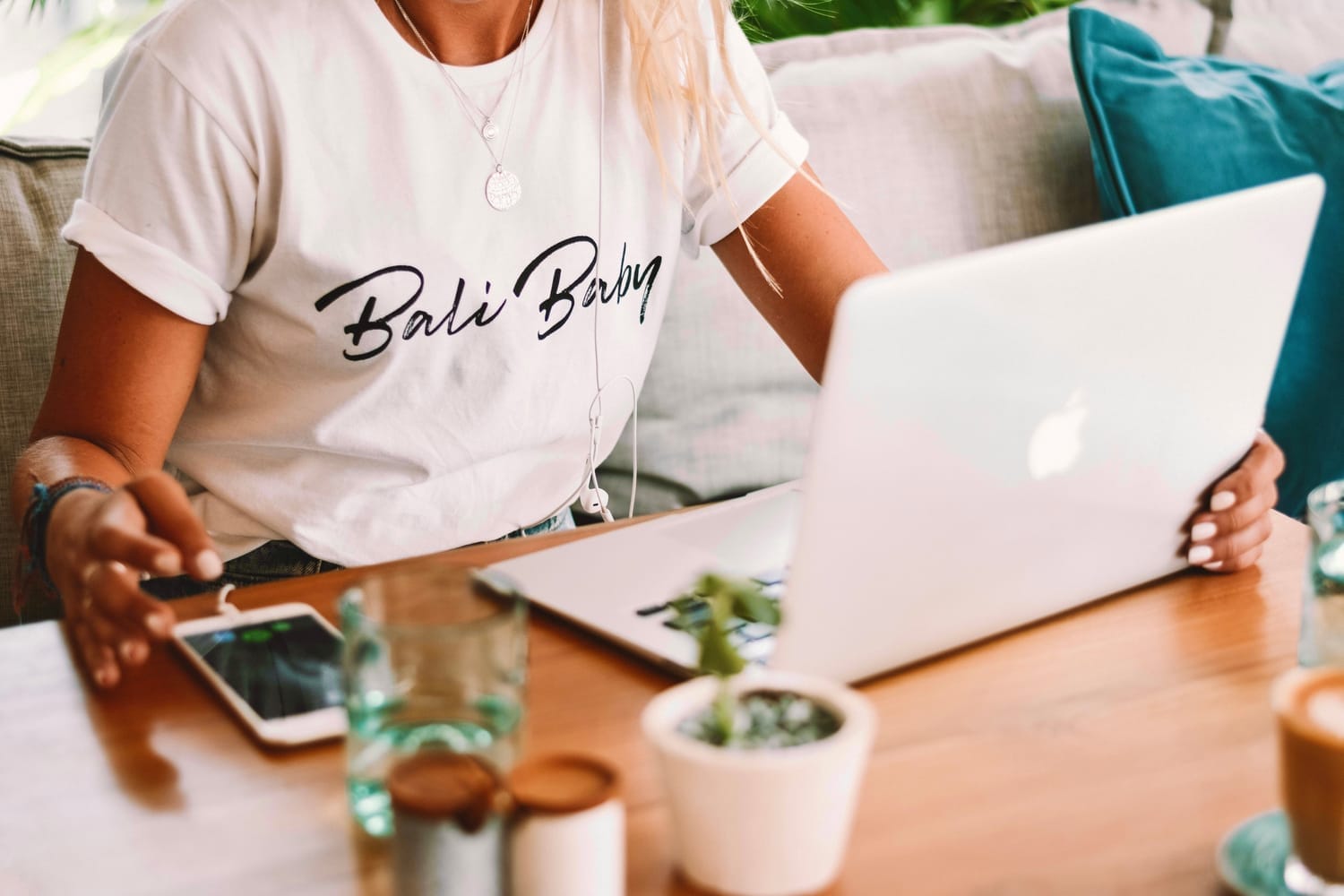 Woman working on a laptop at a wooden table with a plant and coffee
